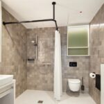 Bis ins kleinste Detail durchdacht, setzen die Bad-Accessoires von HEWI wie die Duschvorhangstange und die Brausehaltestange, der WC-Rollenhalter und die WC-Bürstengarnitur sowie Abfallbehälter edle Akzente in den modern gestalteten Bädern.